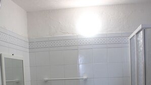 Een kleine badkamer met wastafel, spiegel, toilet, wasmachine en douche.