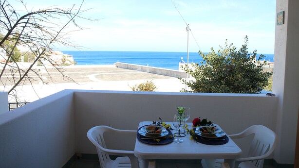 Een balkon met een eettafel voor twee personen, met uitzicht op een strand en de zee.