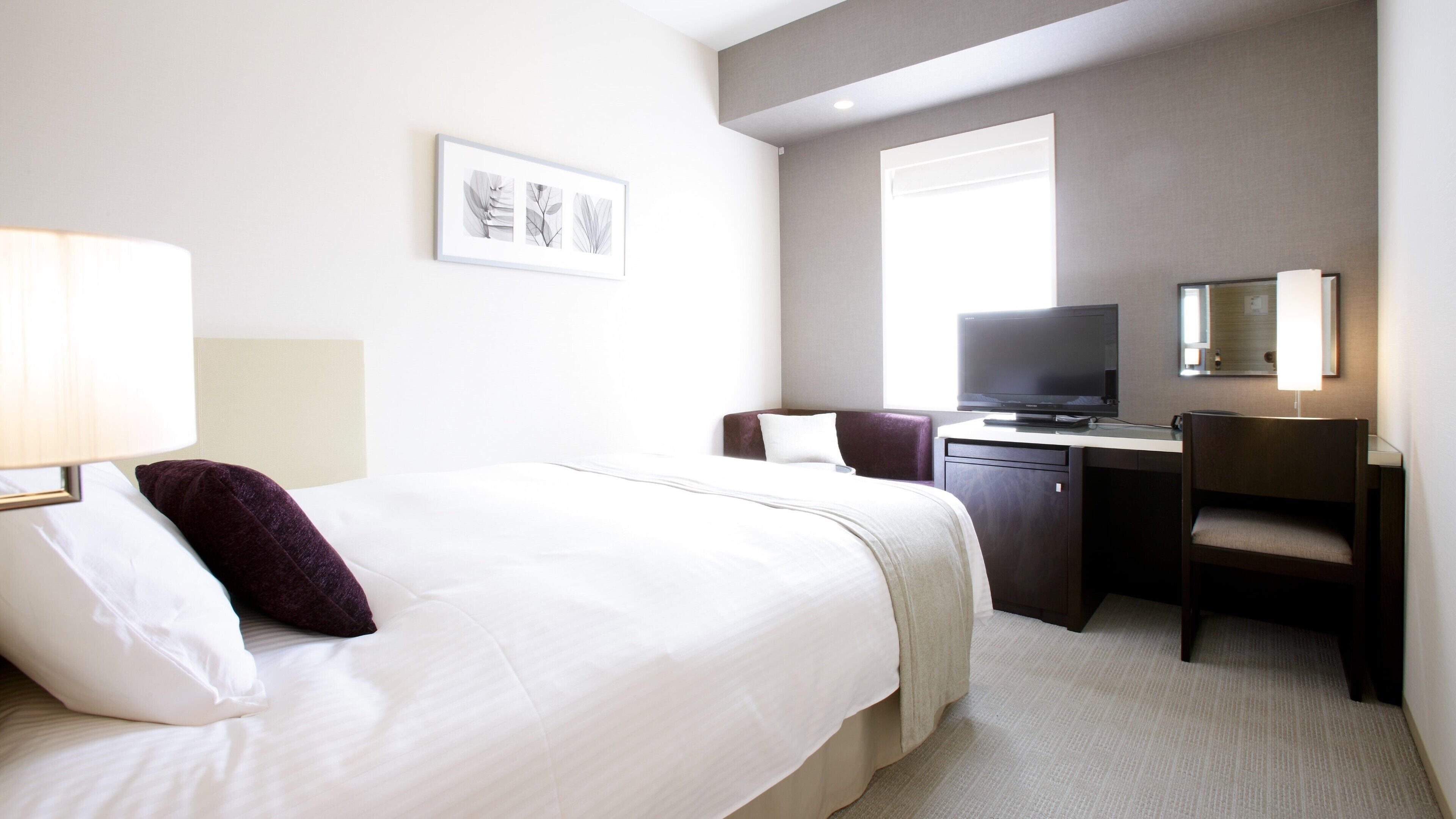 Ein Hotelzimmer mit Bett, Schreibtisch, Stuhl, Fernseher und einem gerahmten Bild an der Wand.