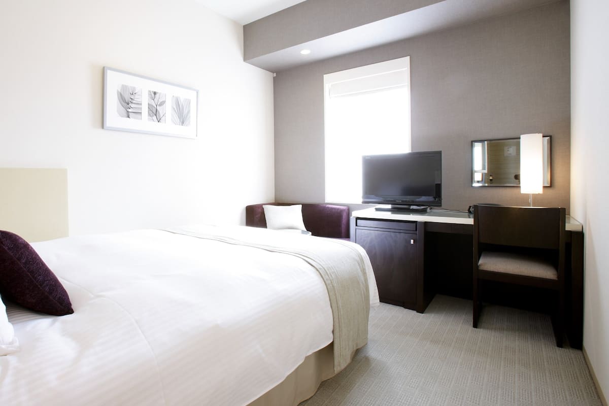 Ein Hotelzimmer mit Bett, Schreibtisch, Stuhl, Fernseher und einem gerahmten Bild an der Wand.