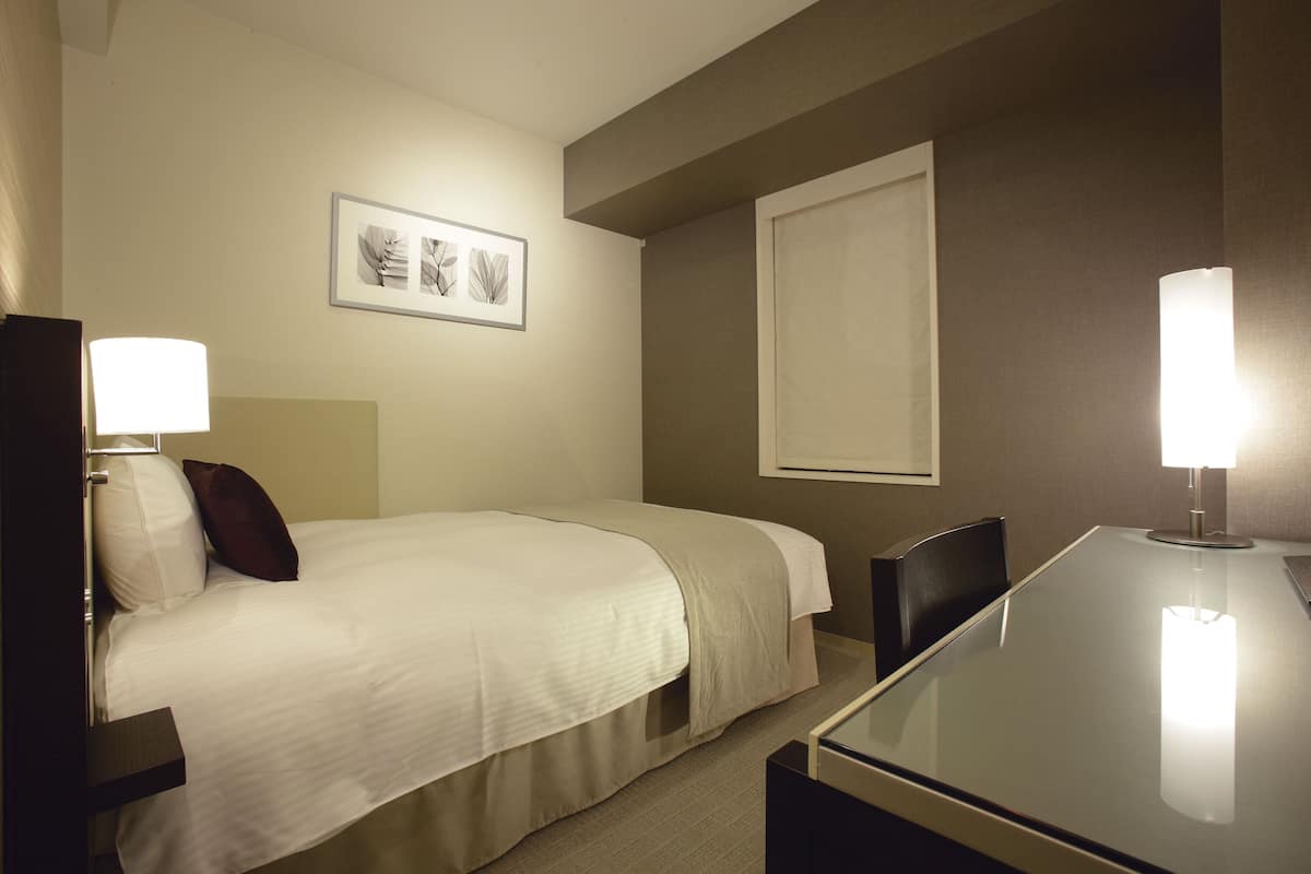 Ein Hotelzimmer mit Bett, Nachttisch, Lampe, Stuhl und einem gerahmten Bild an der Wand.