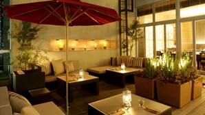 An outdoor seating area with wicker furniture, red umbrellas, and potted plants. - KOKO HOTEL Kobe Sannomiya (Kobe)