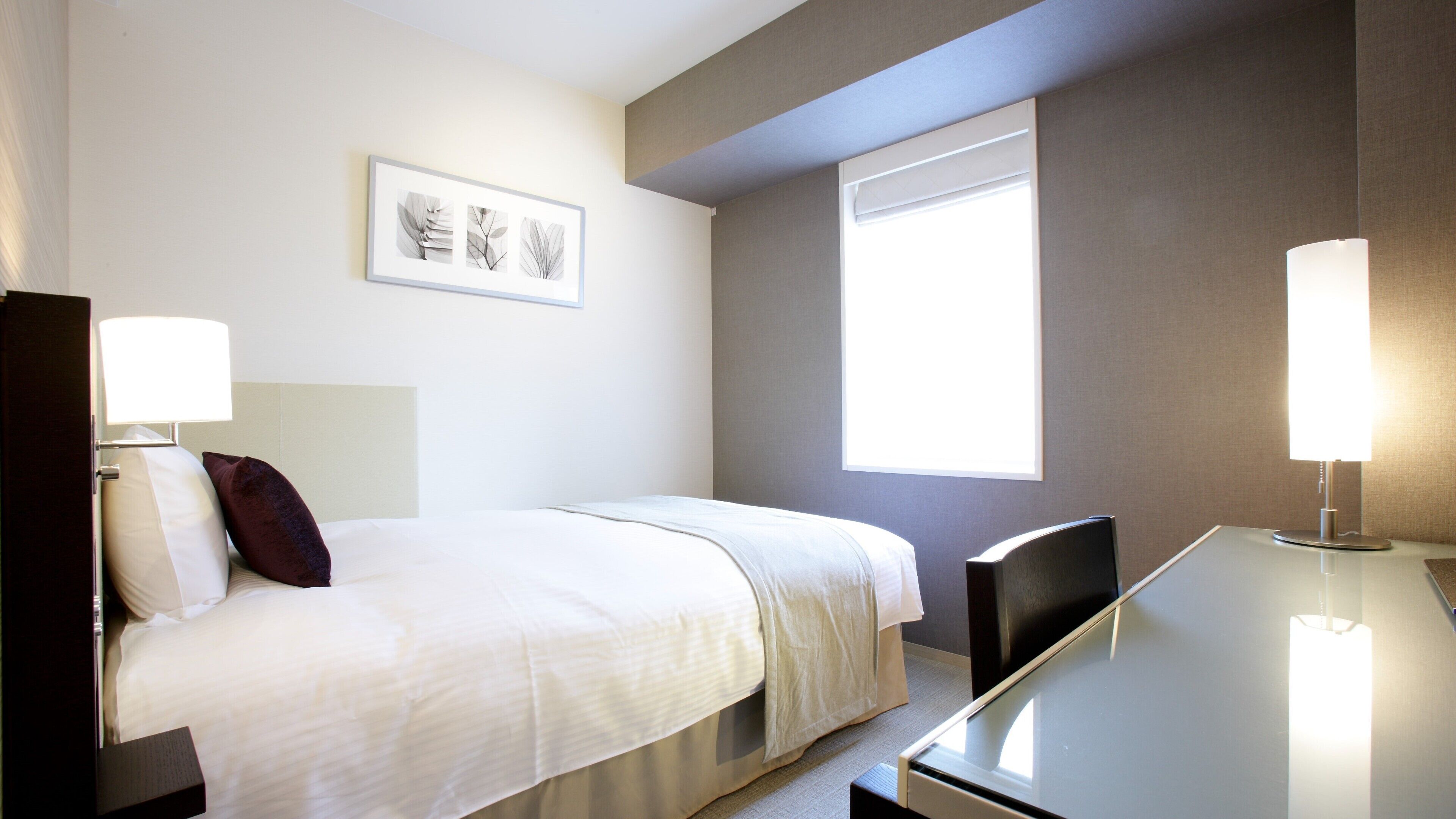 Ein Hotelzimmer mit Bett, Nachttischen, Schreibtisch, Stuhl, Fenster und Wandbildern.