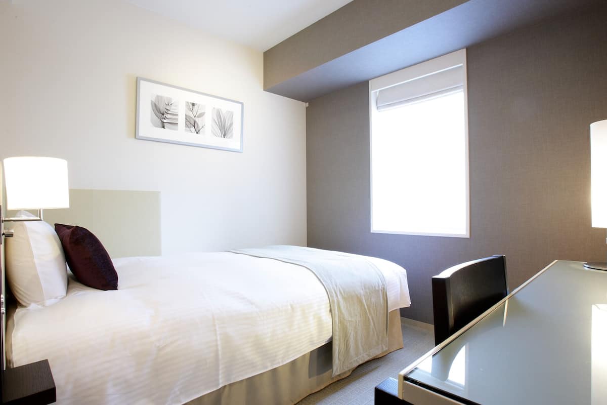 Ein Hotelzimmer mit Bett, Nachttischen, Schreibtisch, Stuhl, Fenster und Wandbildern.
