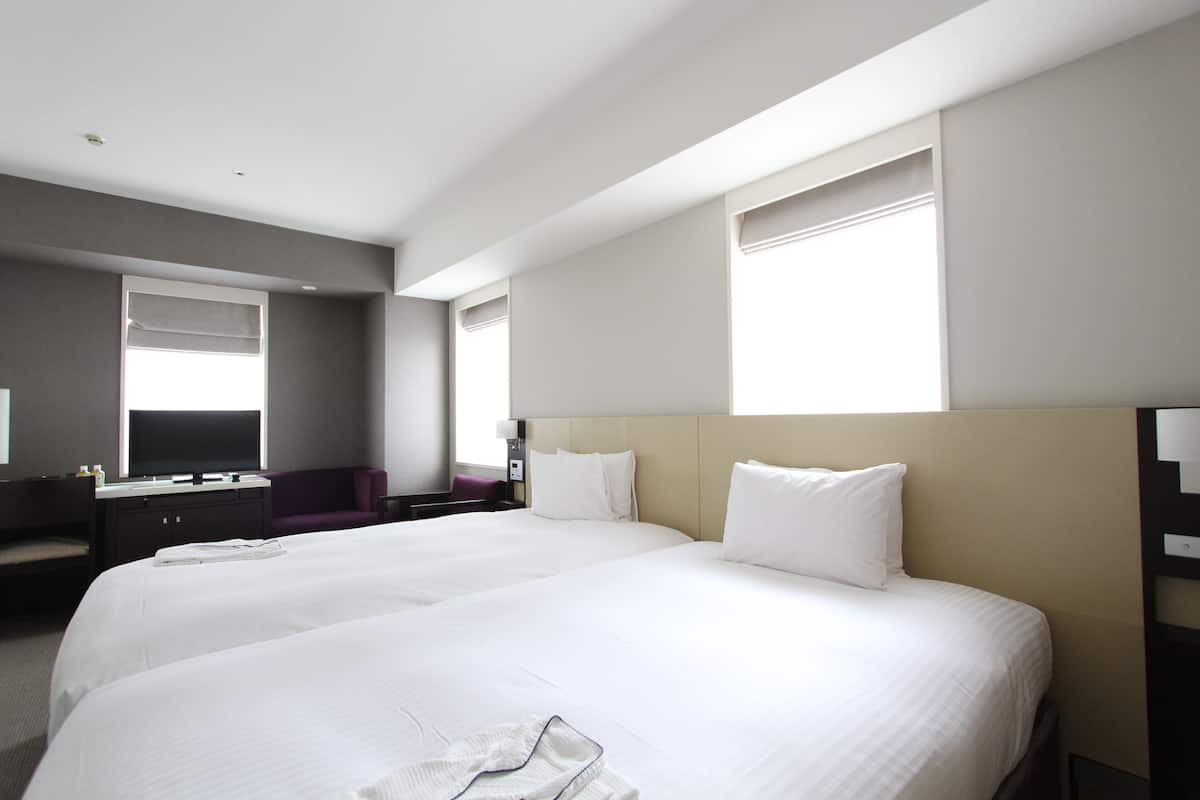 Ein Hotelzimmer mit zwei großen Betten, einem Schreibtisch, einem Stuhl und einem Fernseher.
