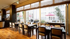 A restaurant with wooden flooring, large windows, and outdoor seating with red umbrellas. - KOKO HOTEL Kobe Sannomiya (Kobe)