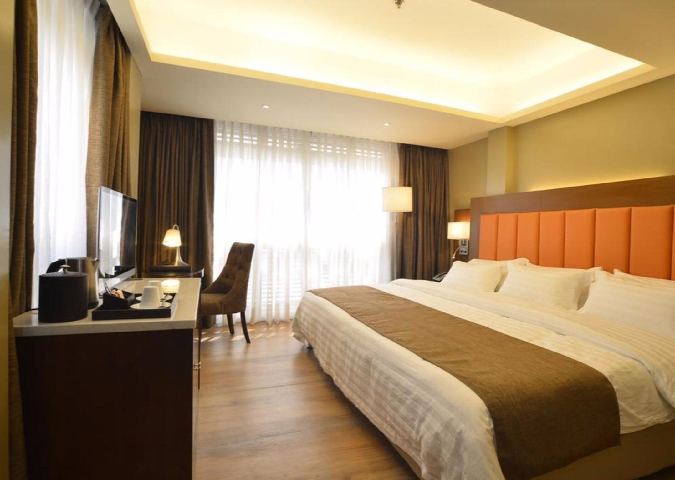 Une chambre d’hôtel avec un grand lit, un bureau avec une chaise, une télévision et une fenêtre avec des rideaux.