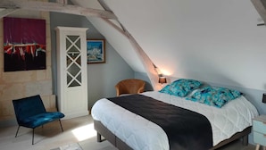Quarto com cama, uma cadeira, um armário branco e um quadro na parede.