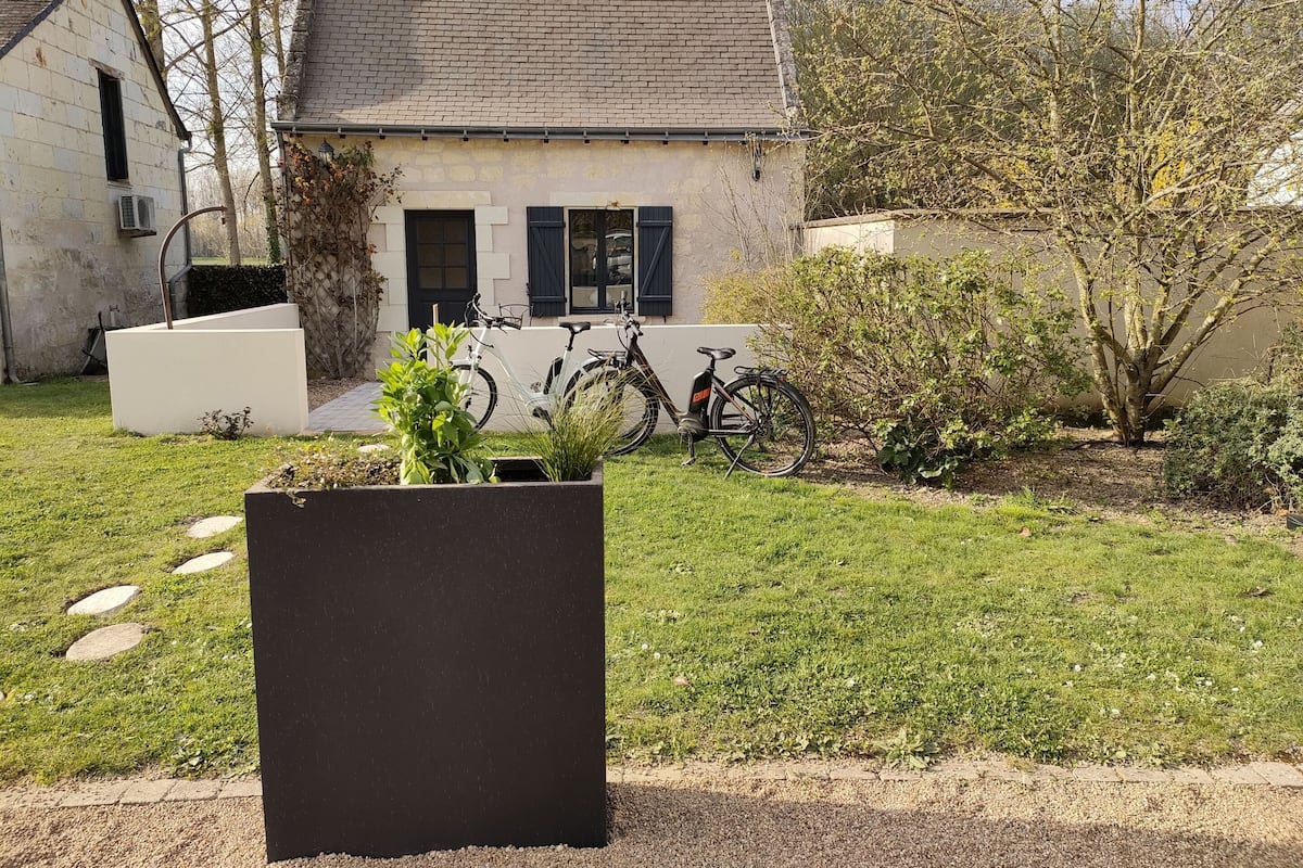 Une maison avec un toit en briques, deux vélos garés devant, et un jardin avec un jardinière au premier plan.