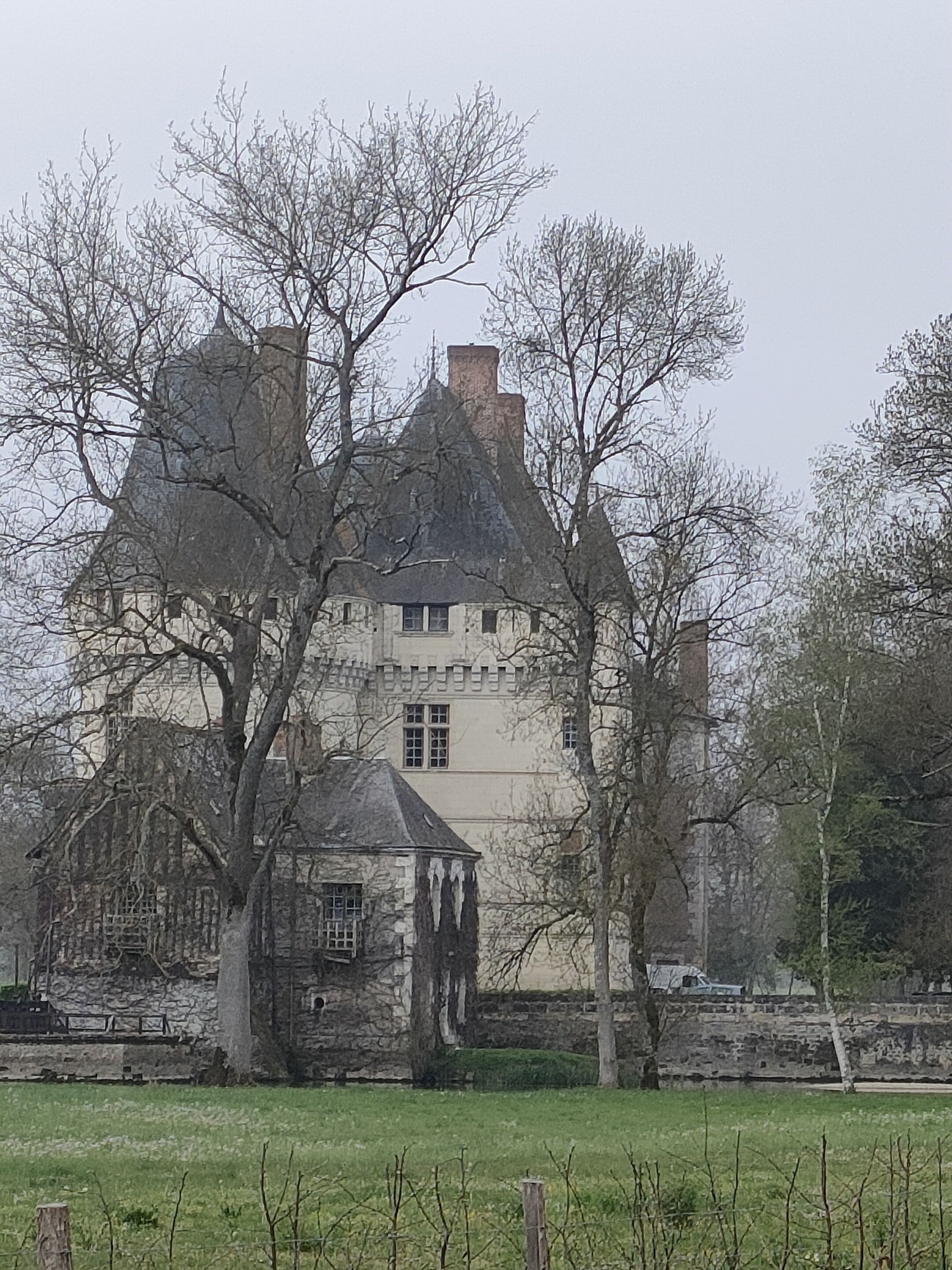 Un edificio de piedra grande e histórico con varias chimeneas, rodeado de árboles y un campo cubierto de césped.