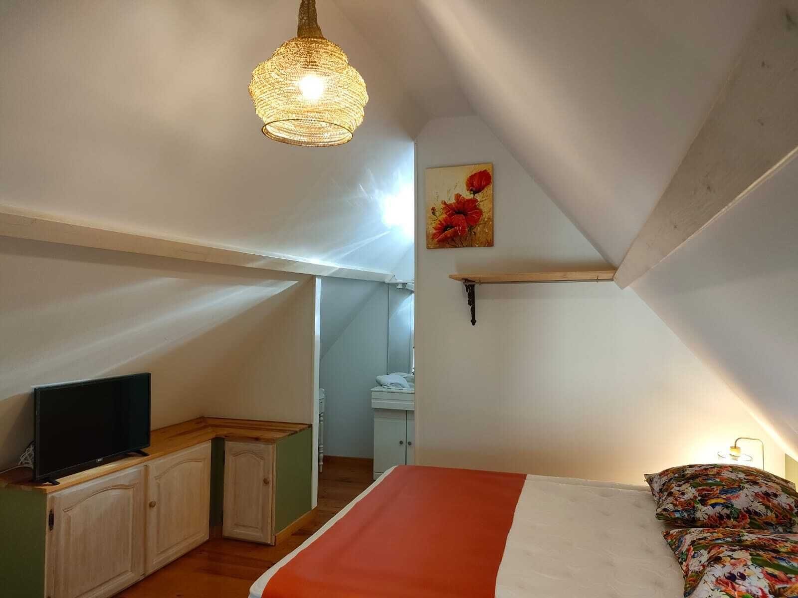A bedroom with a bed, a television on a wooden cabinet, a hanging light fixture, and a painting on the wall.