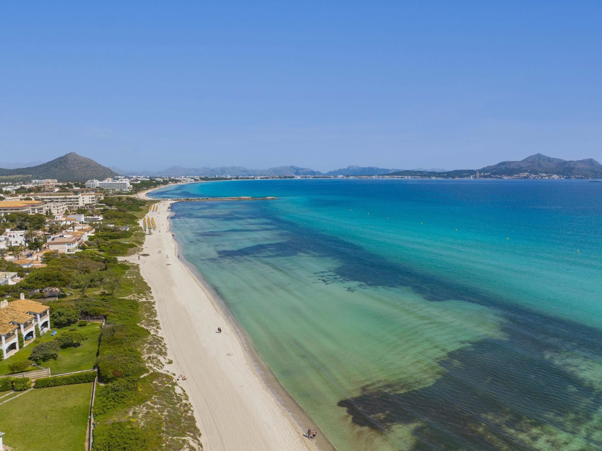 A coastal landscape with a beach, clear waters, and a mountainous backdrop.