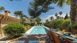 Un espace aménagé au bord de la piscine, avec une table à manger dressée pour un repas, des chaises longues et une vue dégagée sur la piscine.