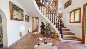 Un magnifique escalier en bois, doté d’une rampe et d’un lustre, mène à un palier agrémenté d’une plante en pot et d’un tapis décoratif.