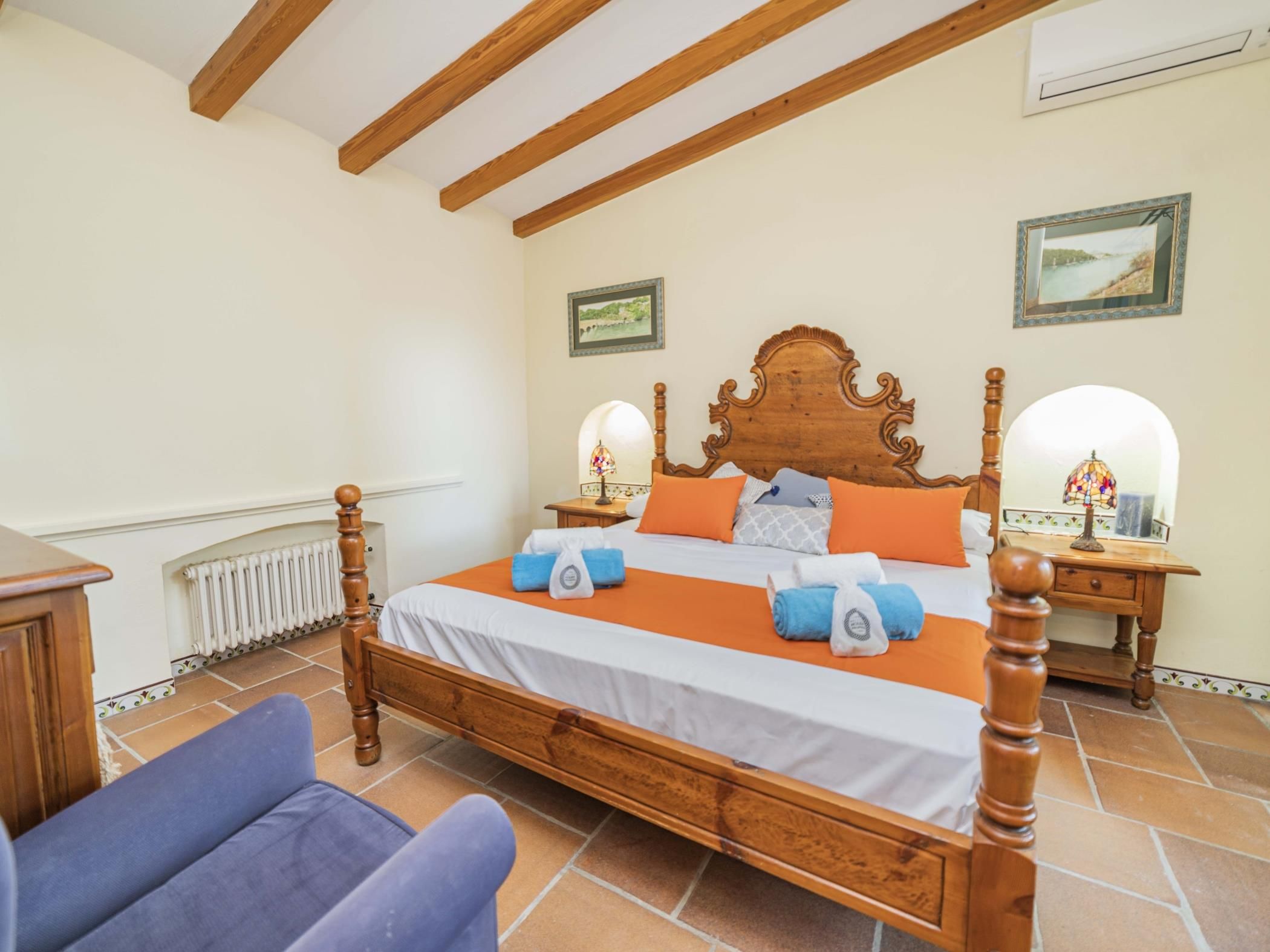A bedroom with a wooden four-poster bed, a nightstand with a lamp, a chair, and a radiator.