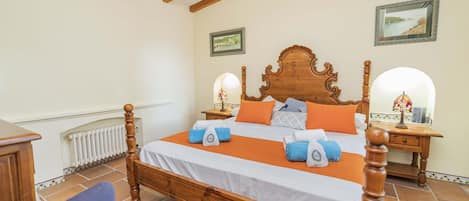 A bedroom with a wooden four-poster bed, a nightstand with a lamp, a chair, and a radiator.