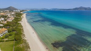 An aerial view of a coastal area with a beach, clear blue waters, and a mountainous backdrop.