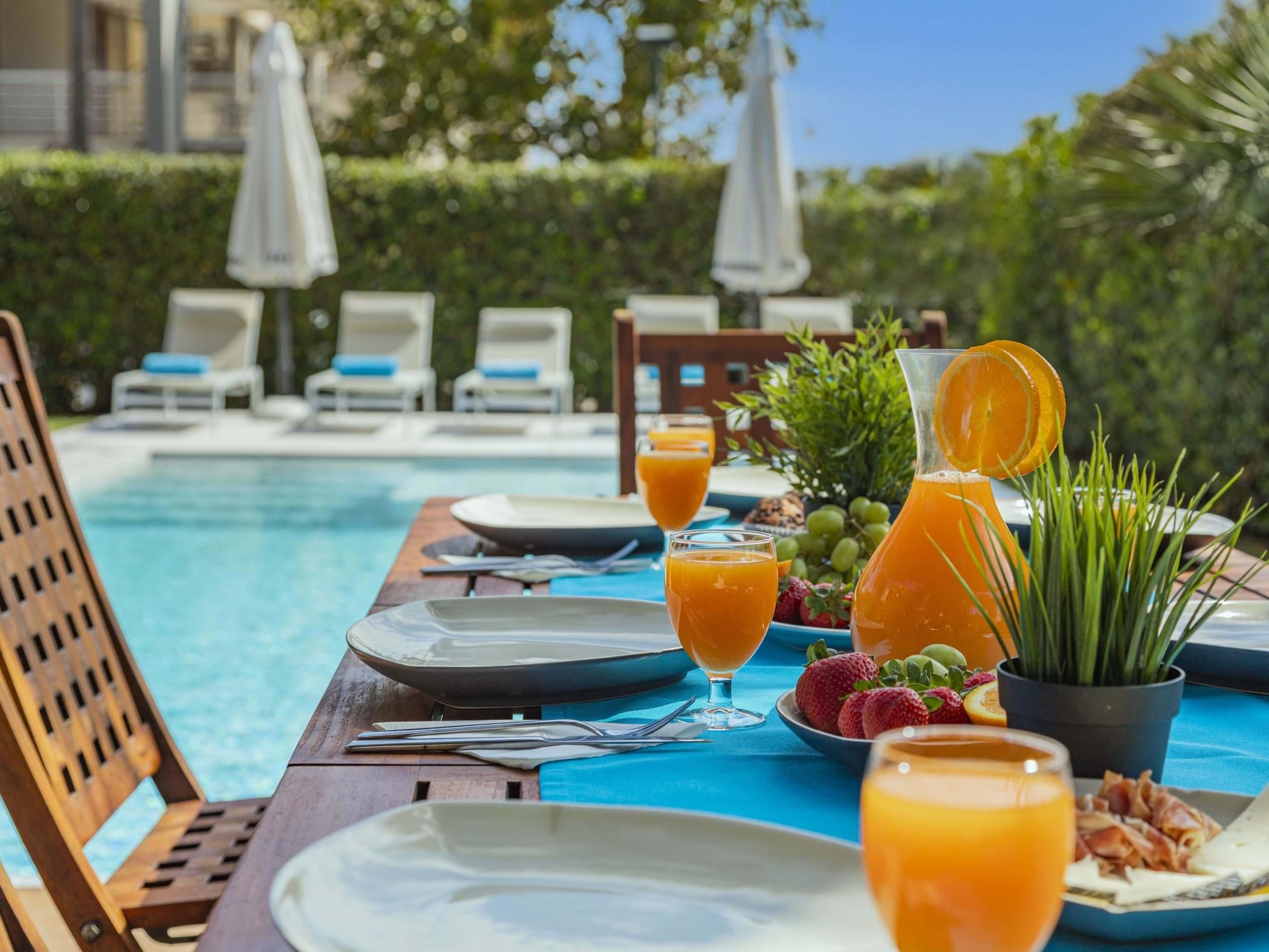 Desayuno junto a una piscina con platos, vasos de zumo de naranja, fresas y una jarra de zumo de naranja.