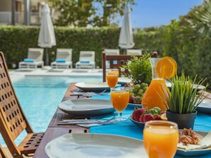 A breakfast setup by a pool with plates, glasses of orange juice, strawberries, and a pitcher of orange juice. - Villa Plomer Serra · Villa with private pool in Playa de Muro (Playa de Muro)
