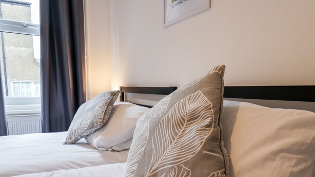 Ein Hotelzimmer mit zwei Betten, jedes mit einem blattgemusterten Kopfkissen und einer weißen Bettdecke.