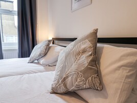 Una camera d'albergo con due letti, ognuno con un cuscino a motivi floreali e una coperta bianca.