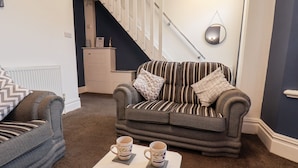 Ein Wohnzimmer mit einem gestreiften Sofa, einem grauen Sessel und zwei Kaffeetassen auf einem kleinen Tisch.