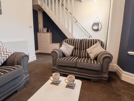 Una sala de estar con un sofá a rayas, un sillón gris y dos tazas de café sobre una mesita.