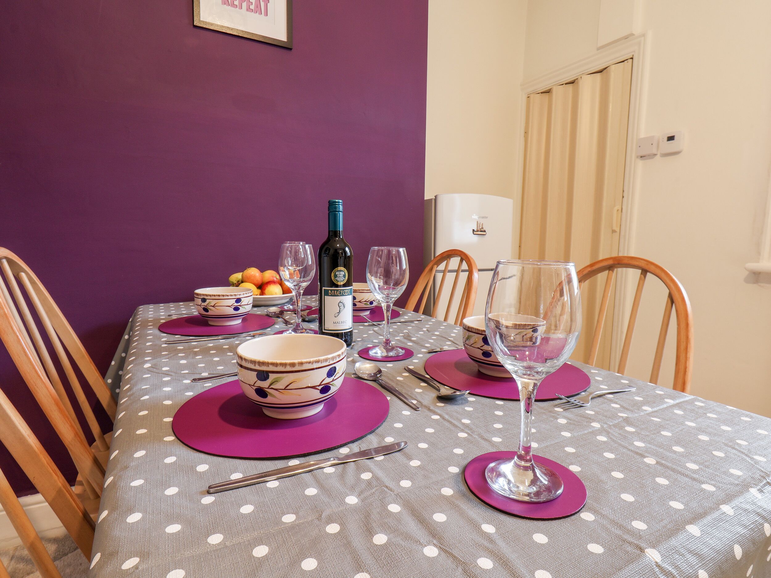 A dining table set with purple placemats, bowls, wine glasses, and a bottle of wine.