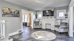 Un salon spacieux avec une cheminée, deux fauteuils, un grand tableau et un téléviseur à écran plat fixé au-dessus de la cheminée.