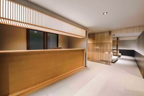 A modern reception area with a wooden reception desk, a seating area with cushions, and a slatted partition. - SKI INN HAKUBA (Otari)