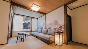 Una habitación con suelo de tatami, techo de madera bajo, un sofá, una mesa y un proyector montado en la pared que muestra una escena de montaña.