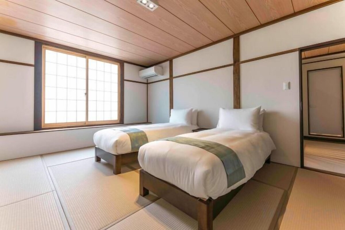 Una habitación de estilo japonés tradicional con suelo de tatami, dos camas con ropa de cama blanca y un puertas correderas.