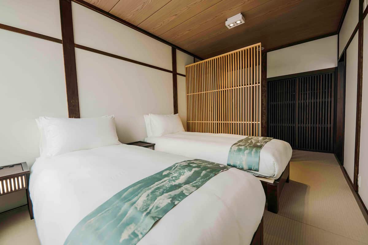 A hotel room with two beds, a wooden ceiling, a shoji screen, and tatami flooring.