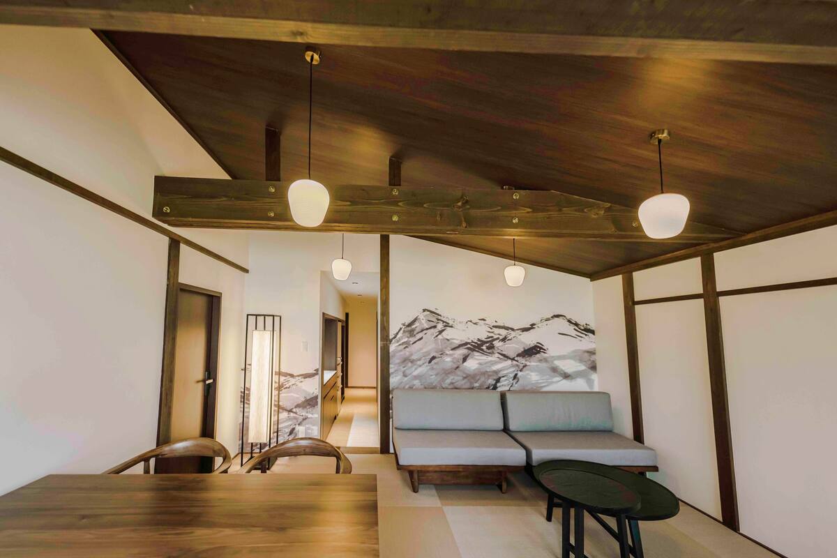 A modern dining area with a wooden table and chairs, a sofa, and pendant lighting.