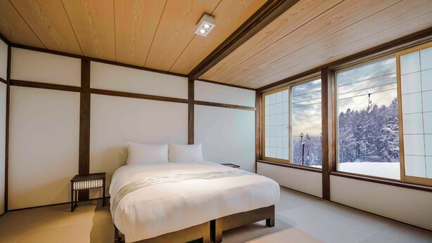 Un dormitorio con una cama grande, una mesita de noche y vistas a un paisaje nevado a través de amplias ventanas.