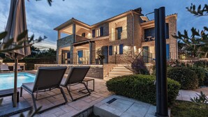 Una casa a più piani con piscina, area salotto esterna e un giardino ben illuminato.