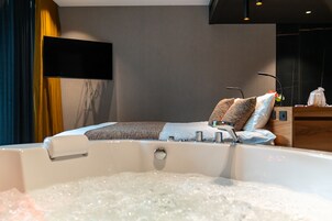 Una habitación de hotel moderna con una cama grande, una bañera con burbujas, un televisor de pantalla plana y una mesita de noche de madera.