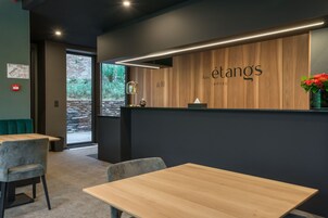 Un área de recepción moderna de hotel con un mostrador de madera, una zona de estar con sillones acolchados y vistas a zonas verdes.