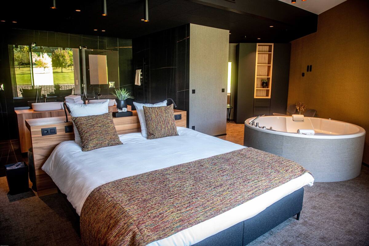 A modern bedroom with a large bed, a sitting area with a sofa and a coffee table, a bathtub, and a bathroom with a sink and mirror.