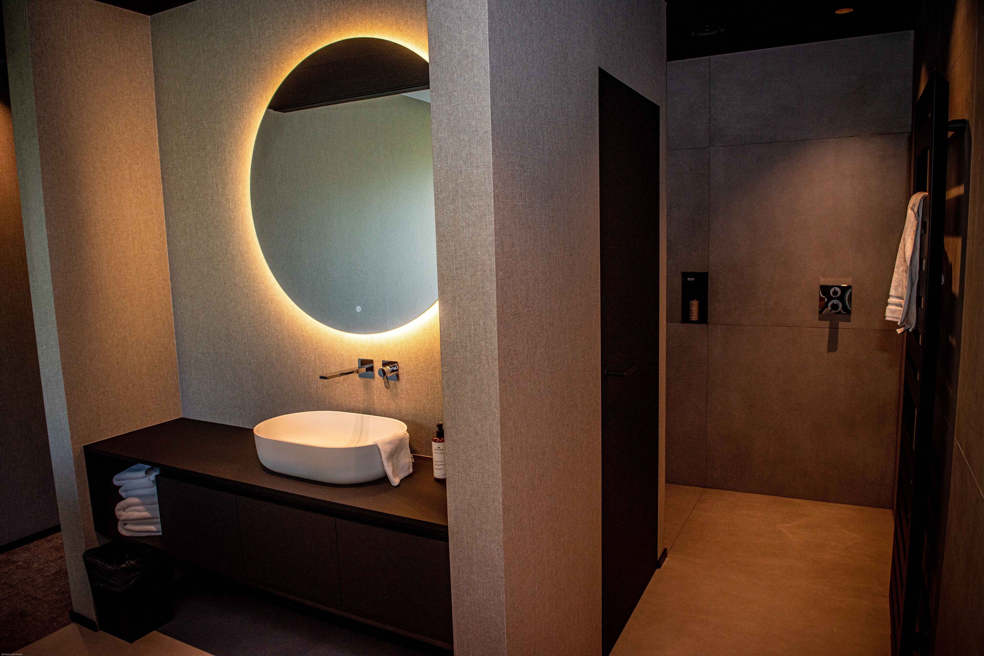 A modern bathroom with a large mirror, a sink, and a shower area.