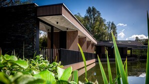 A modern building with a stone facade, wooden panels, and a reflective water feature in front. - Aux Etangs - Hôtel (Herve)