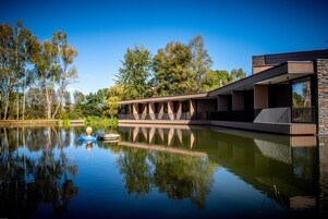 Un edificio moderno con un cuerpo de agua reflectante al frente, rodeado de árboles.