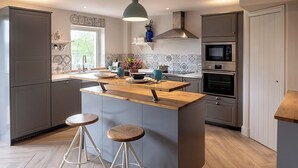 Eine moderne Küche mit grauen Schränken, einer Holzinsel mit Hockern, einem eingebauten Backofen und einer hängenden Pendelleuchte.