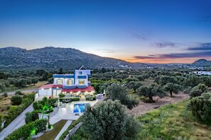 A modern two-story house with a swimming pool, surrounded by olive trees and hills.