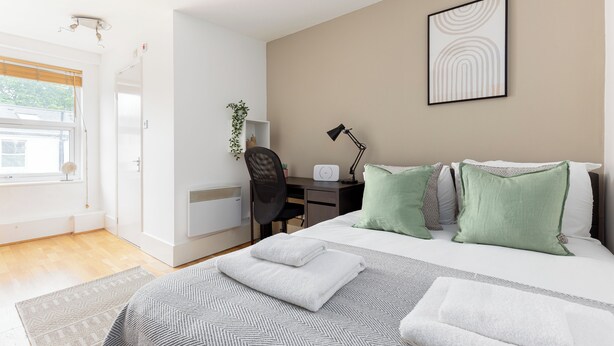 A modern bedroom with a bed, desk, chair, and a view of the outdoors. -  Cosy studio Apartment near Hyde Park (London)