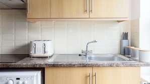 A kitchen with wooden cabinets, a stainless steel sink, a toaster, and a dishwasher. -  Cosy studio Apartment near Hyde Park (London)