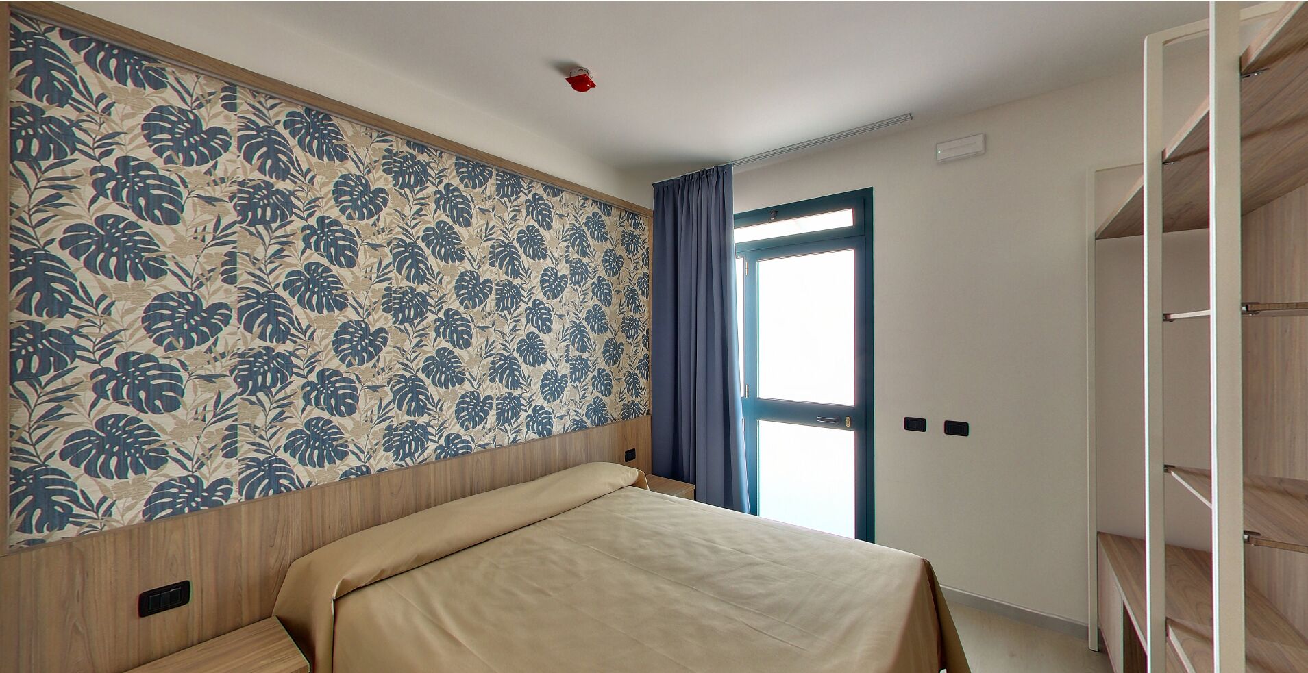 Un dormitorio con cama, armario, ventana con cortinas y pared con estampado floral.