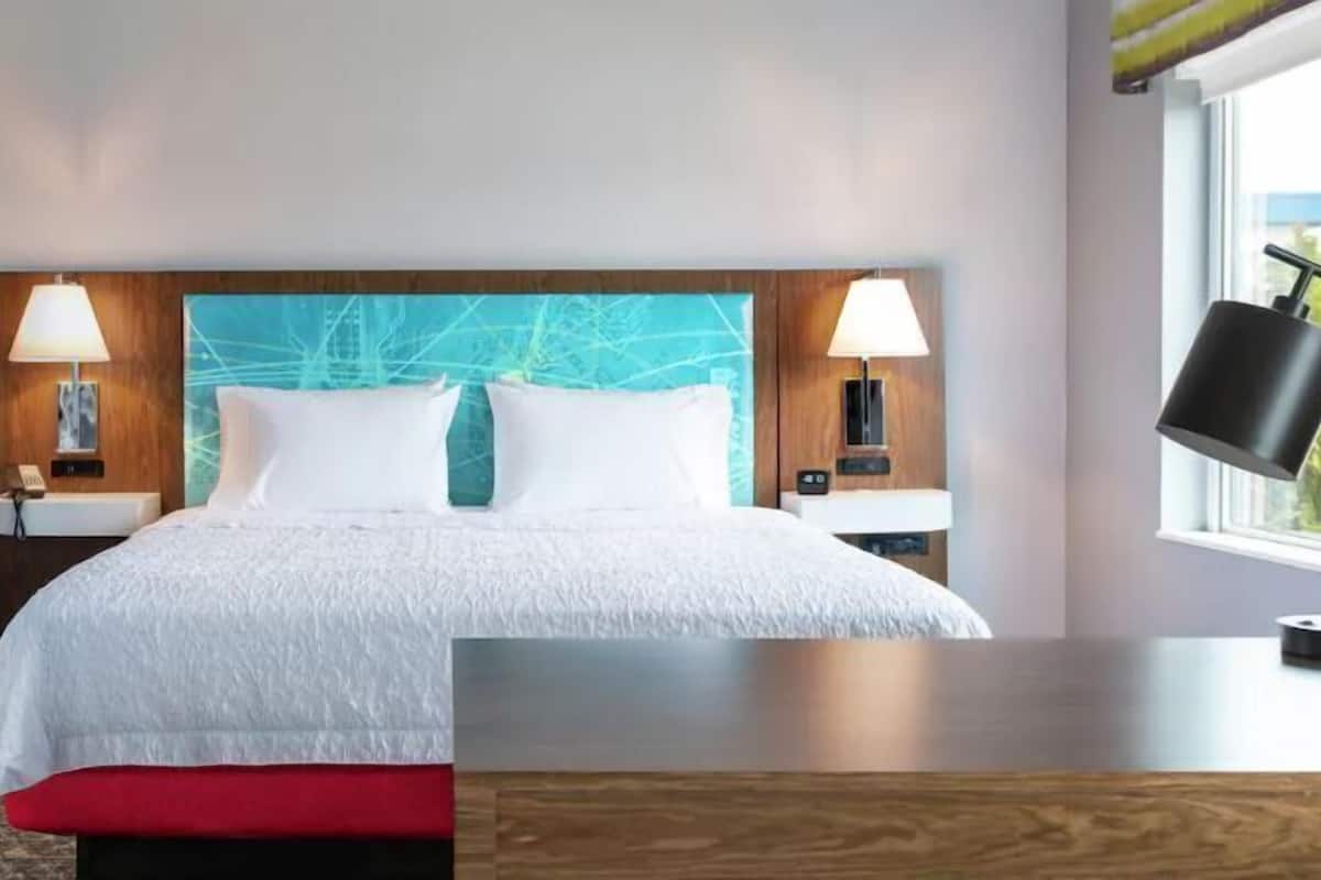 A hotel room with a bed, nightstands, lamps, and a window.