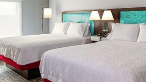 Two double beds with white linens, a wooden headboard with a blue abstract design, and bedside lamps. - Hampton Inn Tappahannock (Tappahannock)