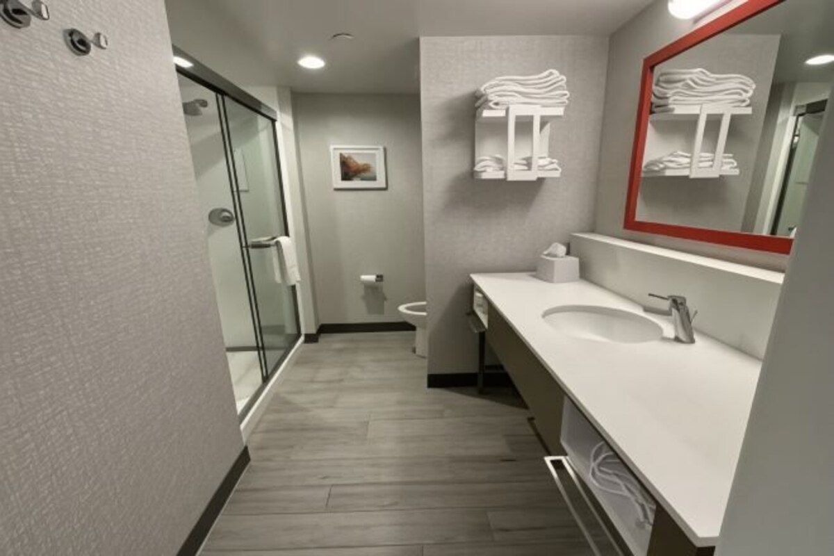 A modern bathroom with a glass shower, a white sink, a large mirror, and a towel rack.